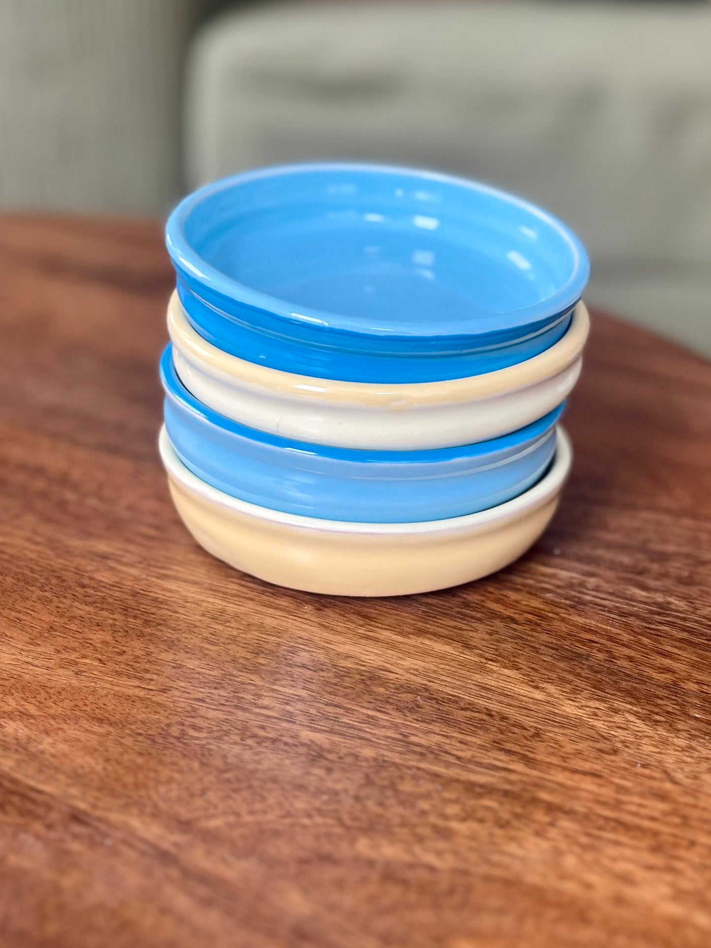 A stack of five small ceramic plates with alternating blue and yellow rims, displayed on a wooden table.