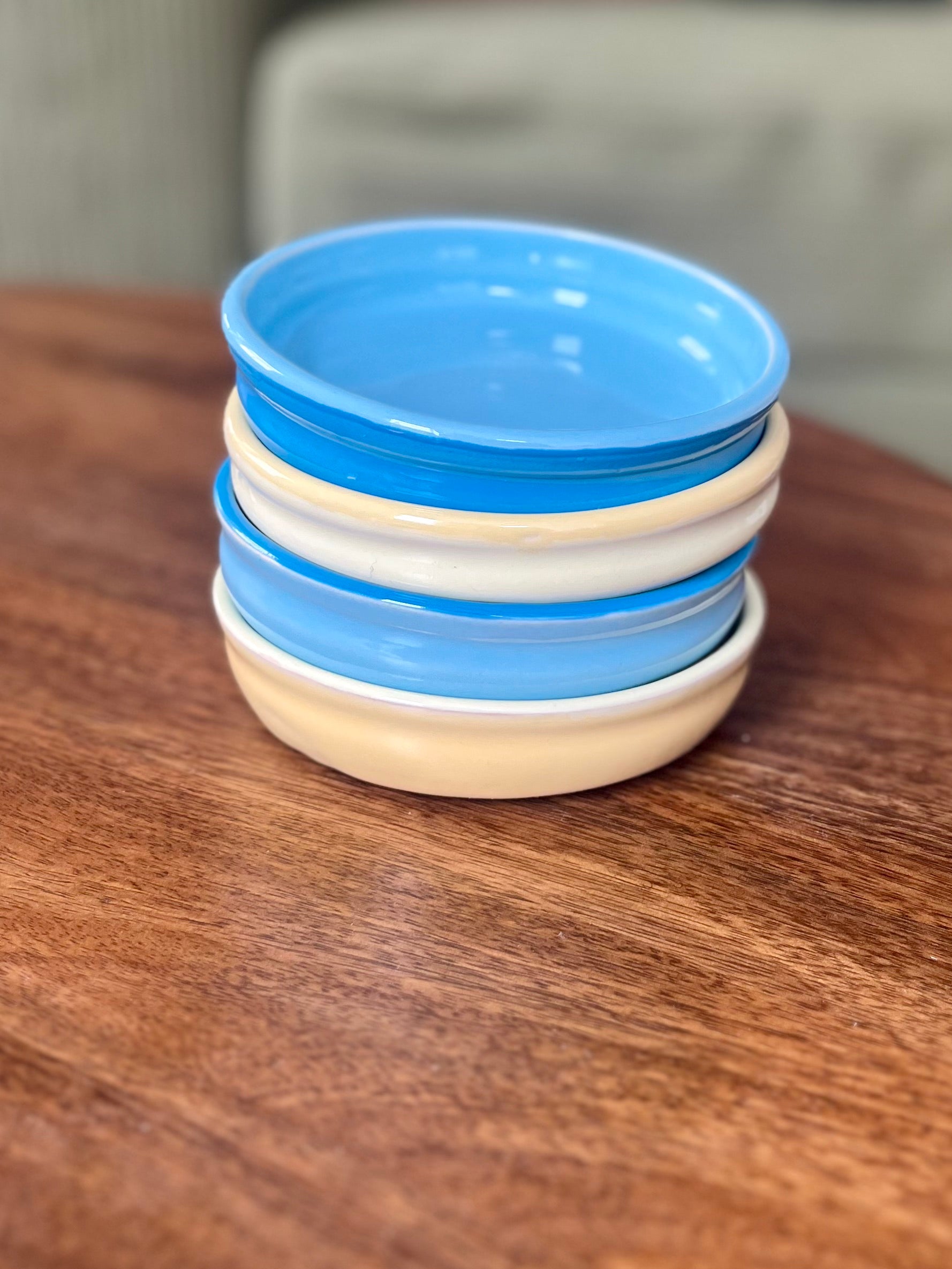 A stack of five small ceramic plates with alternating blue and yellow rims, displayed on a wooden table.