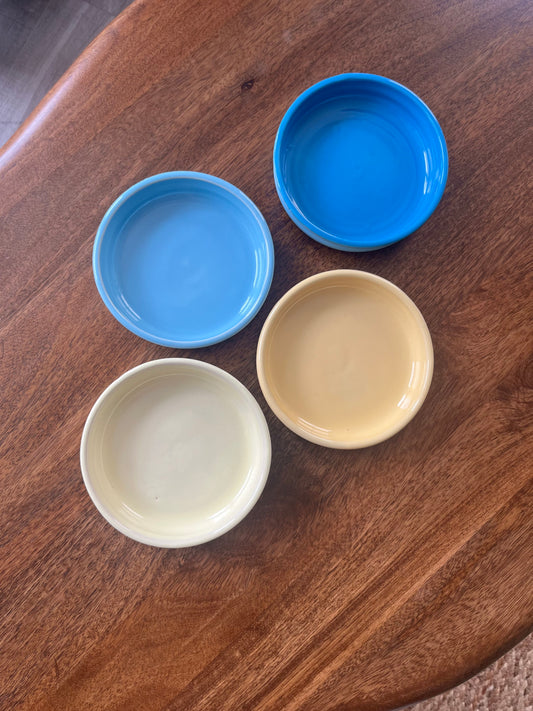 Four small round ceramic bowls in blue, light blue, butter yellow, and pale yellow, arranged on a wooden table.